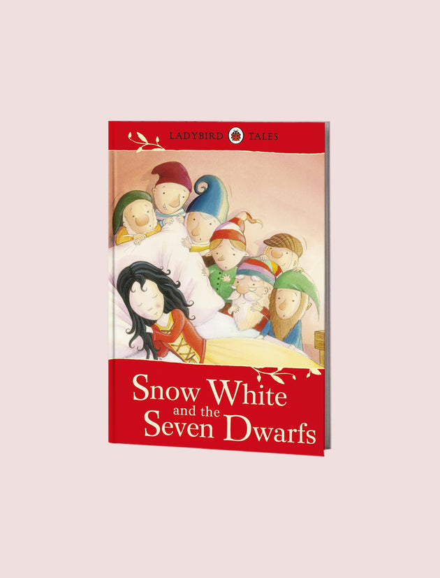 A hardcover book titled 'Snow White and the Seven Dwarfs' from the Ladybird Tales series, shown standing upright against a solid pale pink background.